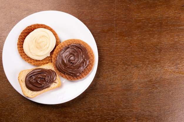 木製のテーブルの上の白いプレートにチョコレートヘーゼルナッツとホワイトチョコレートクリームの上面図でトーストとワッフル