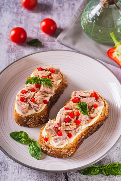 Foto pane tostato con tonno in scatola crema di formaggio peperoni ed erbe aromatiche su un piatto vista verticale