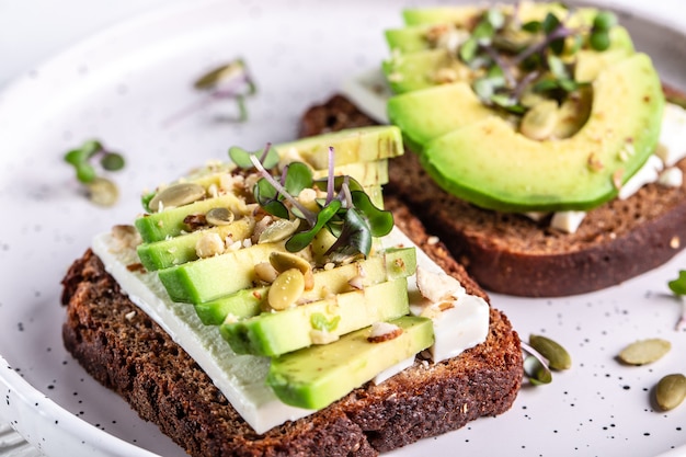 Toast with cheese and avocado on white plate on light surface