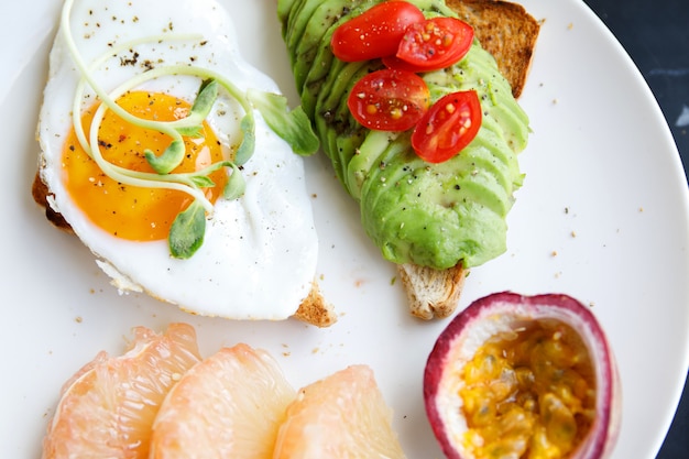 Toast with fried egg avocado and fruits for breakfast