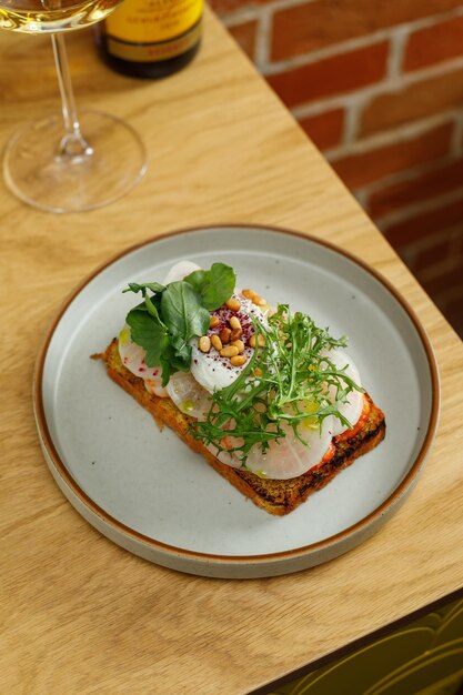 Toast with grilled shrimps and vegetables poached egg and herbs on top served in restaurant Wine bottle and glass on background