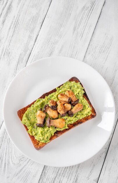 Toast with guacamole and mushrooms on white plate