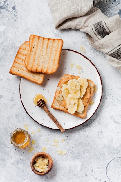 Toast with peanut butter, banana slices, honey and almond flakes on an old gray concrete