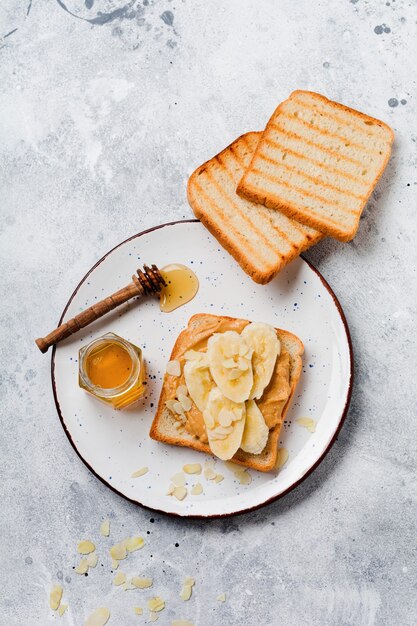 Toast with peanut butter, banana slices, honey and almond flakes on an old gray concrete