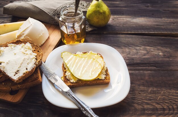 Toast con pera, ricotta e miele su legno rustico con ingredienti.