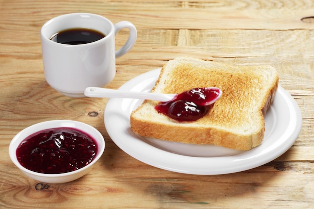 Toast with raspberry jam and cup of hot coffee on old wooden table