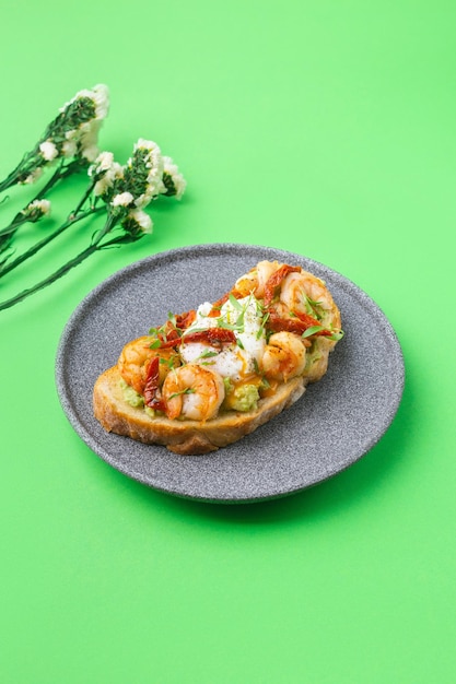 Toast with shrimp prawns avocado and poached egg on green background with flowers high quality photo