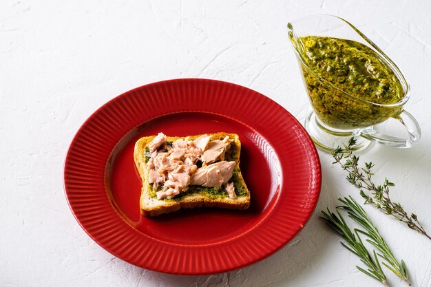 Toast with tuna and chimichurri sauce on a red plate White background