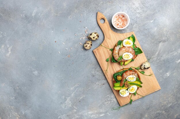 회색 배경에 통밀빵 계란 시금치 아보카도 새우를 곁들인 토스트 케토제닉 아침 슈퍼푸드 개념 건강한 깨끗한 식습관