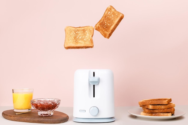 Toasted bread flew out of white toaster near glass of orange juice bowl with strawberry jam