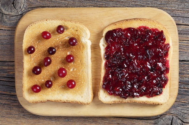 Toasted bread with cranberry jam and berries on kitchen board
