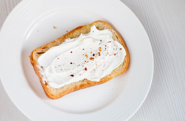 Фото Поджаренный хлеб со сливочным сыром на фоне белой тарелки