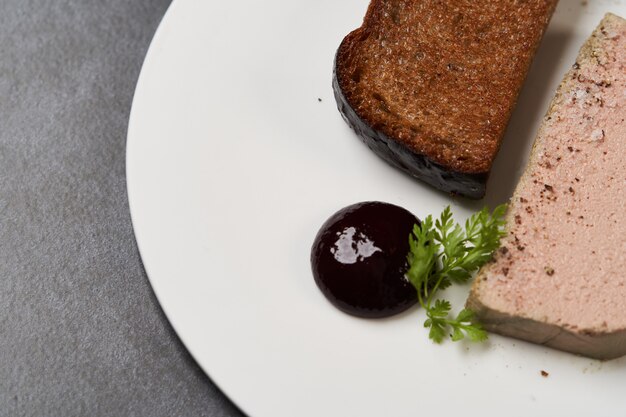 Toasted bread with pate in white plate on dark background with copy space, close-up.