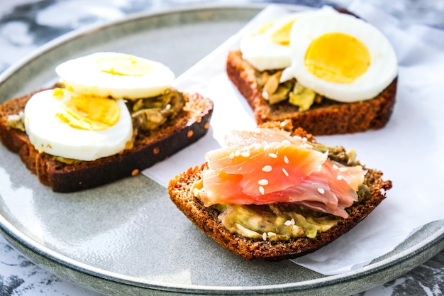 Toasted breads with boiled eggs, avocado and salmon. Guacamole sandwiches. Healthy breakfast. Sesame seeds. Vegetarian healthy eating.