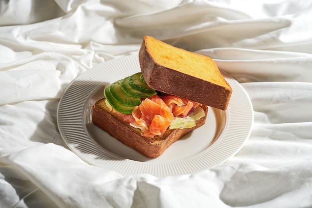 Toasted salmon and avocado sandwich in a plate on a white sheet Tough light