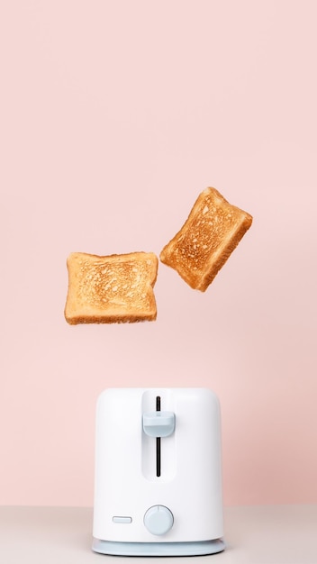 Toasts jumping out of white toaster Levitation food Fresh morning meal Delicious breakfast concept Pink background Copy space Flat lay side view Vertical close up photo