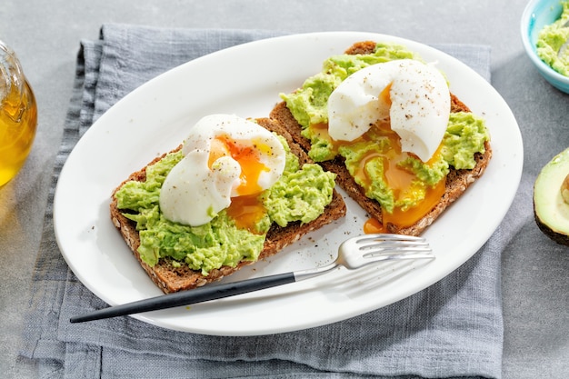 Toasts with avocado and eggs served on plate. Closeup.