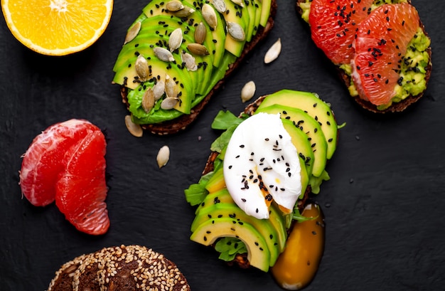 toasts with avocado, sesame seeds, grapefruit, orange, egg and coffee on a concrete black background. delicious breakfast with coffee and toasts