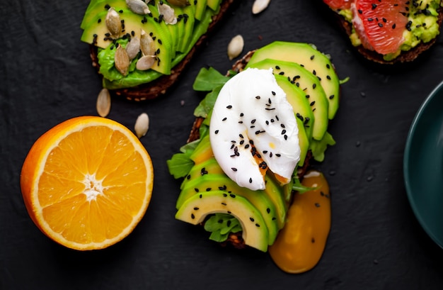 Foto toast con avocado, semi di sesamo, pompelmo, arancia, uovo e caffè su uno sfondo di pietra. deliziosa colazione con caffè e toast