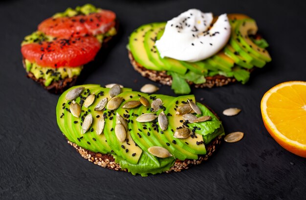 toasts with avocado, sesame seeds, grapefruit, orange, egg and coffee on a stone background. delicious breakfast with coffee and toast