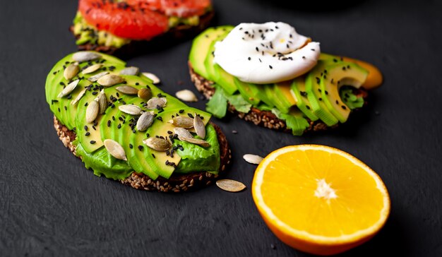 toasts with avocado, sesame seeds, grapefruit, orange, egg and coffee on a stone background. delicious breakfast with coffee and toast