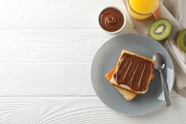 Toasts with choco cream on plate, kiwi and juice on wooden background, top view