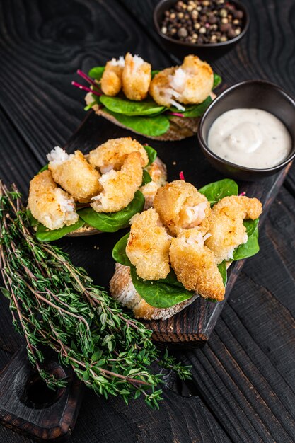 Toasts with Crispy Fried Shrimps  Prawns and green salad on a wooden board. Black wooden background. Top view.