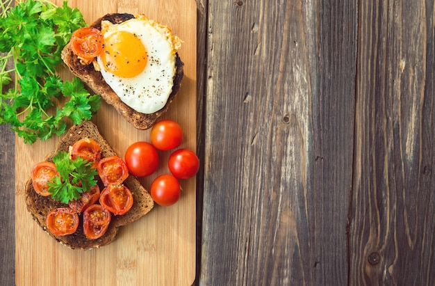 Toasts with egg and fried tomatoes on rustic wooden background. Healthy breakfast.