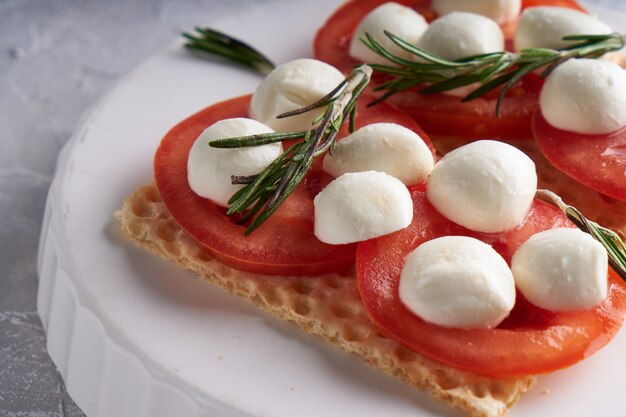 Toasts with mozzarella, tomatoes and rosemary in a white plate