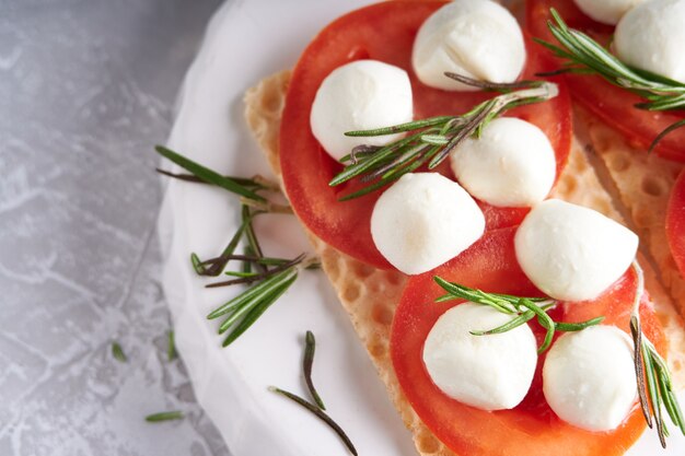Toasts with mozzarella, tomatoes and rosemary in a white plate