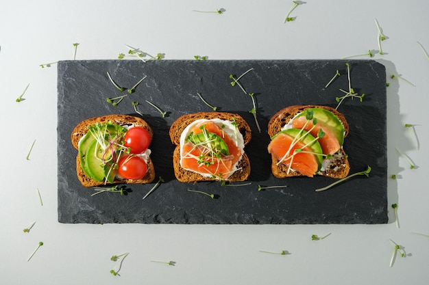 Toasts with salmon trout cherry tomatoes avocado and\
microgreens on black stone board healthy breakfast snack concept\
open sandwiches
