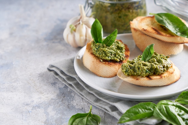 Toasts with traditional Italian basil pesto sauce on a light stone table 