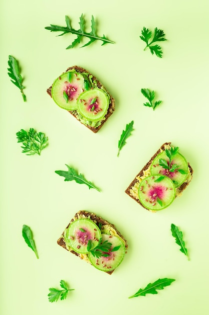 Photo toasts with watemelon radish avocado and flex seeds on color background top view flat lay