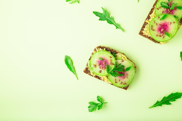 Photo toasts with watemelon radish avocado and flex seeds on color background top view