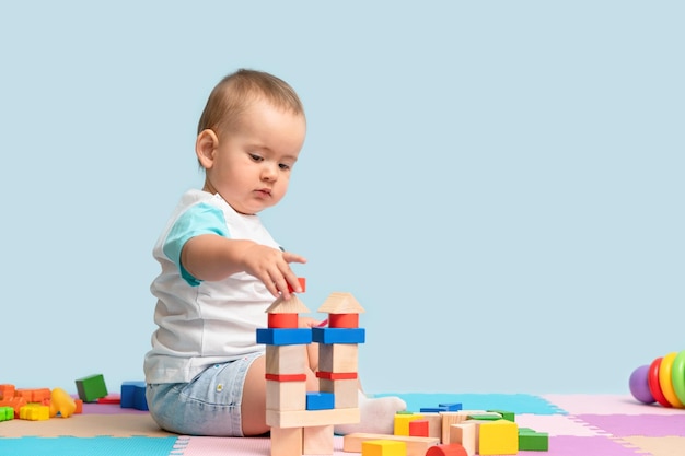 Il bambino di 1217 mesi costruisce una torre di cubi di legno seduti sul pavimento nella stanza dei giochi