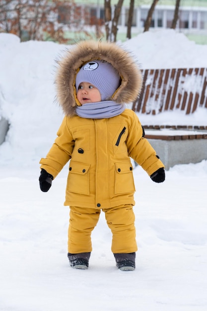 Toddler 1217 months old in yellow winter clothes stands in a winter park and looks sideways