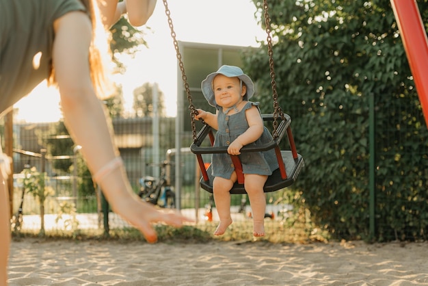 写真 ドレスを着た幼児の女の赤ちゃんが、暖かい夏の夜にブランコに乗って笑っています