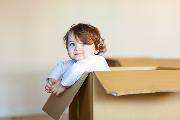 Photo toddler baby girl sitting inside brown cardboard box.