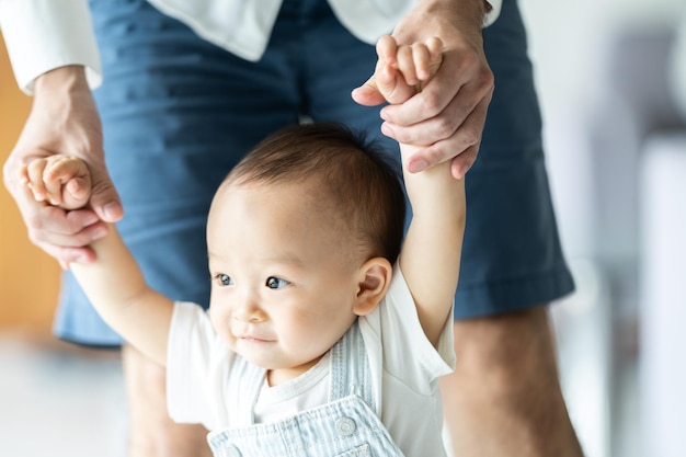 歩き方を学び、家で父と母と一緒に小さな子供と家族のサポートを持っている幼児の赤ちゃんは、助けを借りて歩くことへの第一歩とお父さんから手をつないで幸せな子供時代のヘルプケア