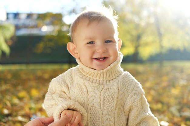 Маленький ребенок играет в осеннем парке, смотрит в камеру и смеется.