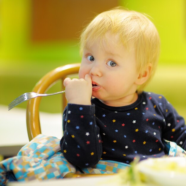 Photo toddler boy eating food at the indoors cafe