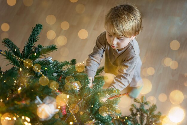 写真 パジャマを着た幼児が家で新年のクリスマスツリーを飾る クリスマスライト