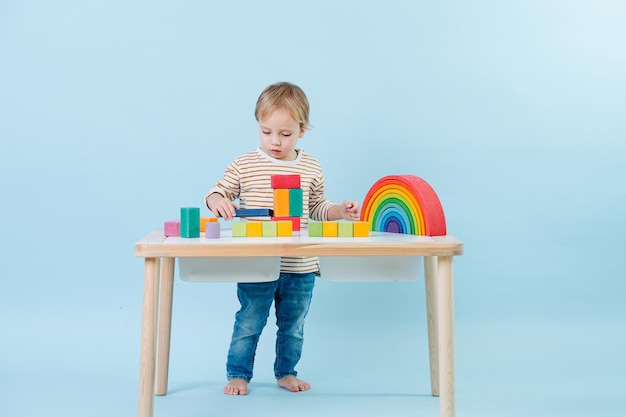 青い背景上のテーブルにカラフルなおもちゃの立方体で遊ぶ幼児の男の子