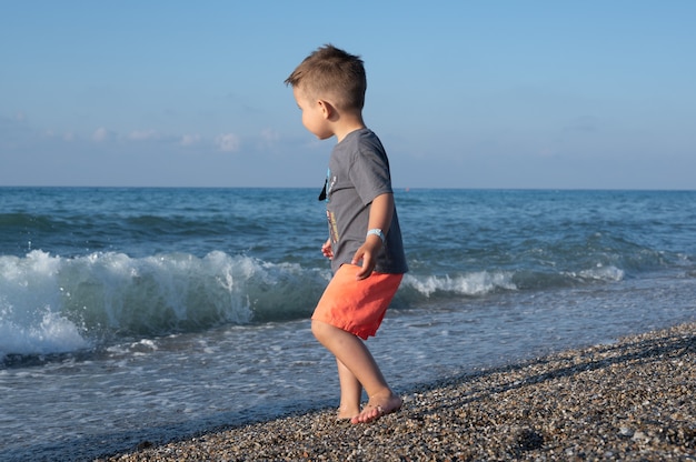 Toddler boy running away from the waves, small boy alone on the beach.