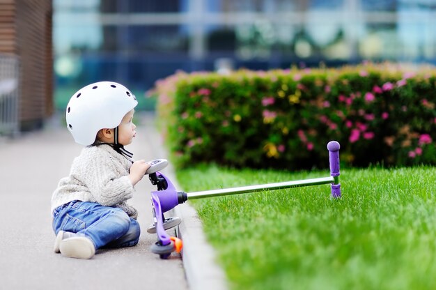 Toddler boy in safety helmet learning to ride scooter