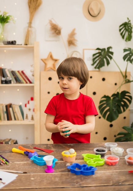 Toddler boy sculpts from plasticine at the table in the room