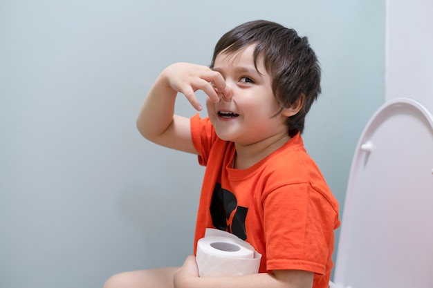 Toddler boy sitting in the toilet and covers his nose from the smell