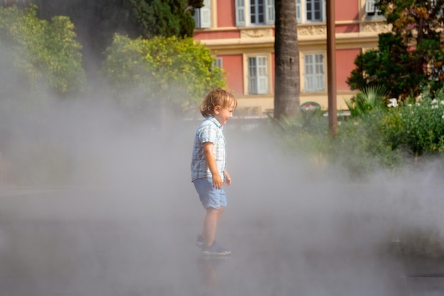 Toddler boy under spray jets of extensive water mirror fountain\
in nice france pleasant refreshment stay coll in summer heat