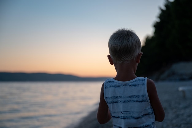 Foto bambino in piedi sulla spiaggia la sera