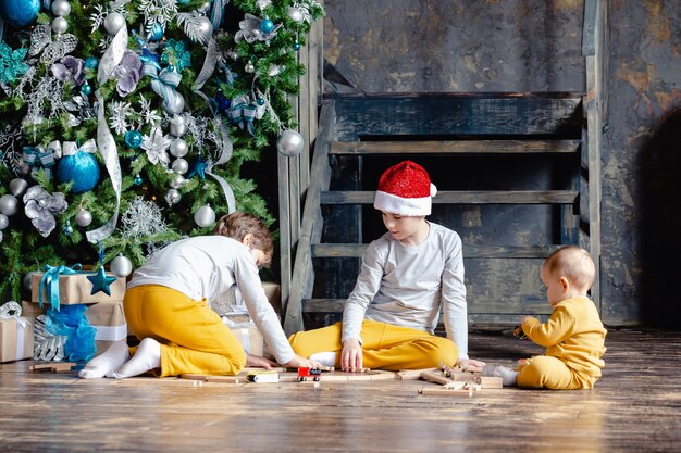 Ragazzi del bambino con la ferrovia della costruzione del cappello della santa e che giocano con il trenino sotto l'albero di natale. bambini con regali di natale. periodo natalizio.